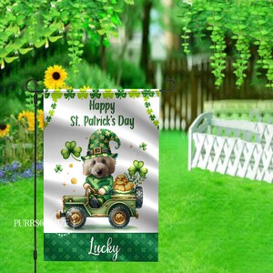 May include: A white garden flag with a green shamrock pattern. It features a cartoon dog wearing a green leprechaun hat and driving a green jeep. The text "Happy St. Patrick's Day" and "Lucky" are on the flag.