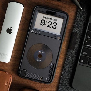 Könnte beinhalten: Eine schwarze Sony Walkman-ähnliche Handyhülle mit einem weißen Bildschirm, der die Uhrzeit 9:23 und den Text "向上轻扫描以解锁" in Chinesisch anzeigt. Die Hülle hat einen kreisförmigen Ausschnitt, der einem CD-Player ähnelt.