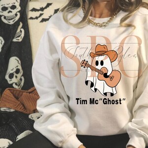 May include: White long-sleeve sweatshirt with a graphic of a ghost wearing a cowboy hat and playing a guitar. The text "Tim Mc "Ghost"" is printed below the graphic.