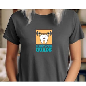 May include: A dark gray t-shirt with a white tooth lifting a barbell. The tooth is smiling and has blue eyes. The text "I like your quads" is printed below the tooth.