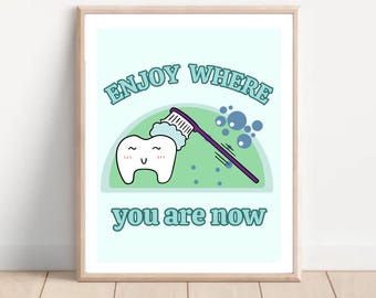 May include: A light blue and green printable wall art design with a cartoon tooth being brushed with a toothbrush and bubbles. The text reads "Enjoy where you are now".