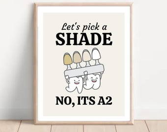 May include: A white framed poster with a dental humor design. It features two cartoon teeth holding a shade guide and the text "Let's pick a SHADE NO, IT'S A2".
