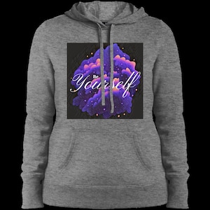 Puede incluir: Una sudadera con capucha gris con un bolsillo en la parte delantera. El gráfico en la parte delantera es un diseño abstracto morado y naranja con el texto "Be Yourself" en blanco.