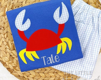 Könnte beinhalten: Ein blaues T-Shirt mit einer roten und gelben Krabben-Applikation. Das Shirt ist mit dem Namen "Tate" personalisiert.