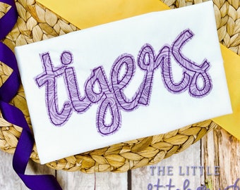 May include: Purple "tigers" text with a swirl pattern on a white fabric background.