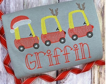 May include: A gray shirt with a red and yellow embroidered design of three toy cars. The first car has a Santa hat, and the other two have antlers. The name "Griffin" is embroidered in red below the cars.