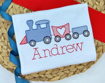 Könnte beinhalten: Ein weißes T-Shirt mit einem gestickten Design eines blauen Zuges mit einem roten Güterwagen und dem Namen "Andrew" in rotem Garn.