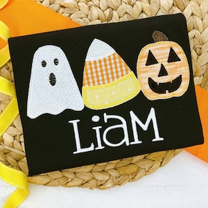 May include: Black Halloween shirt with a ghost, candy corn, and jack-o-lantern applique. The shirt says "Liam" in white.