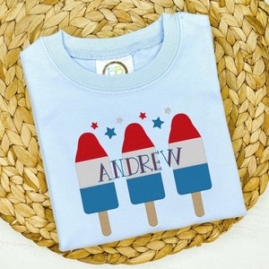 Könnte beinhalten: Hellblaues T-Shirt mit drei roten, weißen und blauen Eis am Stiel-Grafiken und dem Namen "ANDREW" in schwarzem Text.