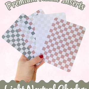 May include: A hand holds four rectangular Kindle inserts with checkerboard patterns in gray, white, and pink. The text "Premium Kindle Inserts" and "Light Neutral Checker" are displayed in a cursive font.