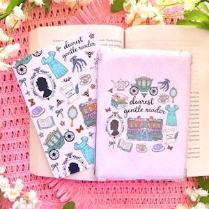 May include: Two pink book covers with the text "dearest gentle reader" and various illustrations, including a silhouette, dress, carriage, and teacup. The covers are on top of an open book and pink fabric, with white flowers in the background.