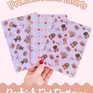 May include: Three Kindle inserts with pastel pink backgrounds and pet-themed patterns. One features a checkerboard pattern with paw prints and flowers. The others have cats and dogs with books and bows. Text reads "Premium Kindle Inserts" and "Bookish Pet Patterns."