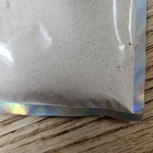 May include: A white powder in a clear plastic bag with a holographic iridescent border.