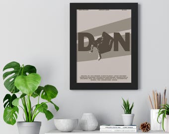 Può includere: Un poster incorniciato con una cornice nera. Il poster presenta la grande parola "DON" in marrone scuro, con una figura reclinata su una striscia diagonale. Il poster ha testo in alto e in basso.