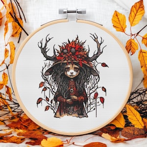 Könnte beinhalten: Kreuzstichmuster mit einer fantasievollen Figur mit Geweih, einem rot-braunen Hut und einem dunkelroten Kleid. Die Figur hat einen traurigen Ausdruck und ist von Herbstblättern umgeben.