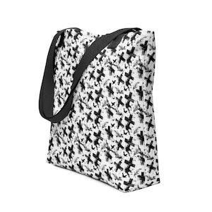 May include: White tote bag featuring a black cross pattern, bird silhouettes, and sprig designs. It has a black shoulder strap. The bag is made of a durable material.