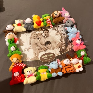 May include: A 10 inch by 8 inch photo frame with a family photo inside. The frame is decorated with a variety of colourful stuffed animals, including bears, frogs, and a monkey.