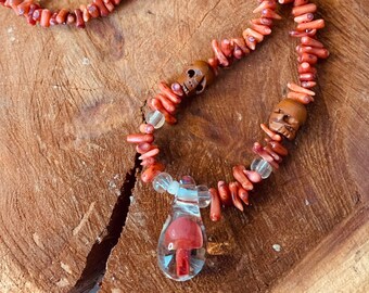 May include: A red coral necklace with two wooden skull beads and a glass pendant containing a red mushroom.