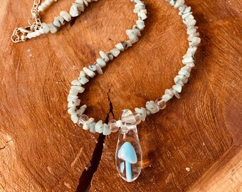 May include: A light blue and white crystal necklace with a glass mushroom pendant. The necklace is made of small, irregular shaped stones.