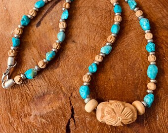 May include: A turquoise and wood bead necklace with a carved wooden flower pendant. The necklace is made of alternating turquoise and wood beads.