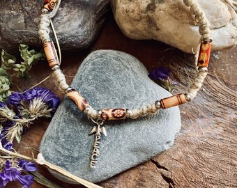 May include: A hemp cord necklace with wooden beads and a silver peace sign charm. The beads are painted with floral patterns in shades of brown, orange, and red.