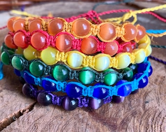 May include: A set of six colorful bracelets with different colored beads and cords. The bracelets are stacked on top of each other, creating a rainbow effect. The bracelets are made with natural materials and have a bohemian style.