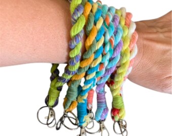 May include: A set of six colorful braided keychains with silver key rings. Each keychain is made of a different color combination of yarn, including green, yellow, orange, blue, and purple.