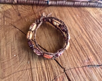 May include: A brown leather bracelet with brown and orange beads. The bracelet is wrapped around itself twice.