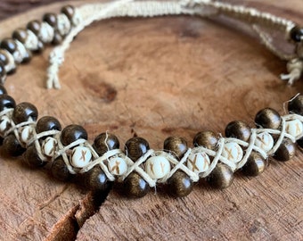 May include: A brown wooden bead necklace with white beads and a natural fiber cord. The necklace is woven with a criss-cross pattern.