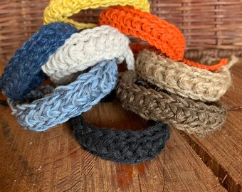 May include: A set of eight crocheted bracelets in various colors, including yellow, orange, beige, blue, and brown. The bracelets are made of a thick, textured yarn and are stacked on top of each other.