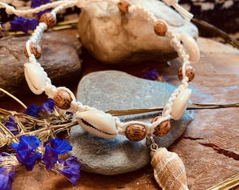 May include: A white macrame cord bracelet with brown wooden beads and white seashells. The bracelet has a large seashell charm hanging from it.