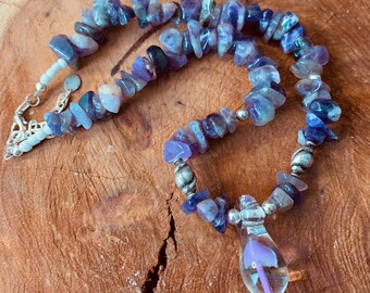 May include: A purple and blue gemstone necklace with a silver clasp and a glass pendant shaped like a mushroom.