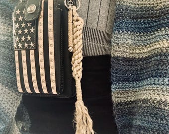 May include: A black phone case with a white and black American flag design. The case has a strap and a white tassel keychain.
