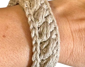 May include: A beige crocheted bracelet with a braided design. The bracelet is made of thick, textured yarn and has a simple, elegant style.