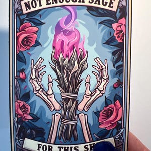 May include: A vintage-style card with a blue background and floral accents. The card features a skeletal hand holding a bundle of sage with pink flames. The text on the card reads "NOT ENOUGH SAGE FOR THIS SH", suggesting a magical or spiritual theme.