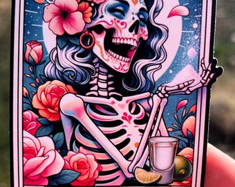 May include: A tarot card with a colorful illustration of a skeleton woman with a sugar skull face, wearing a flower crown and holding a shot glass of tequila. The card is titled "The Salty B*tch".
