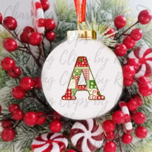 Peut inclure: Boule de No&euml;l blanche avec une lettre A en patchwork rouge, vert et blanc. La boule est entour&eacute;e de baies rouges et de cannes en sucre.
