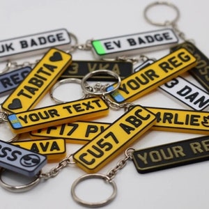 May include: A collection of yellow and black personalised keychains with different names and text. The keychains are shaped like number plates and have a silver chain.