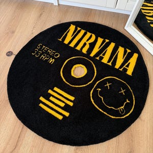 May include: Black round rug with yellow text and graphics. The word "NIRVANA" is across the top. Below the word "NIRVANA" are the words "STEREO 33 RPM". A yellow smiley face and other yellow graphics are also on the rug.