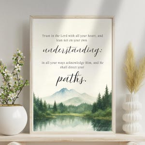 May include: A framed print with a watercolour landscape scene featuring a lake, mountains, and trees. The print includes the text "Trust in the Lord with all your heart, and lean not on your own understanding: in all your ways acknowledge Him, and He shall direct your paths."