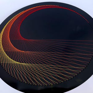 May include: A circular piece of black wood with a geometric design created with red, orange, and yellow thread. The thread is strung between small nails that are evenly spaced around the circle.