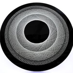 Puede incluir: Una pieza de arte de pared circular negra con un diseño geométrico blanco. El diseño es una serie de círculos concéntricos con un patrón de cuadrícula blanca.