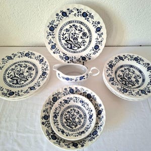 Könnte beinhalten: Eine Sammlung weißer Keramik-Geschirr mit blauem Blumendesign. Das Set umfasst Teller in verschiedenen Größen und eine Sauciere. Die Teller haben einen gewellten Rand und ein detailliertes Muster aus Blumen und Vögeln.