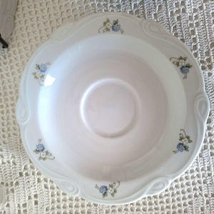 Könnte beinhalten: Weißer Porzellan-Servierteller mit gewelltem Rand und zarten floralen Akzenten. Die Schale hat kleine blaue und weiße Blumengruppen um den Rand. Das Design ist klassisch und elegant, geeignet zum Servieren oder Ausstellen.