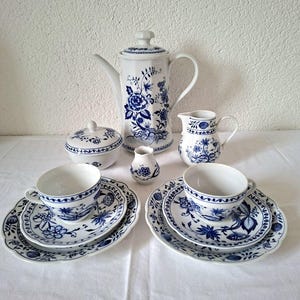 Könnte beinhalten: Ein komplettes blau-weißes Porzellan-Teeservice. Das Set beinhaltet eine Kaffeekanne, eine Zuckerdose, einen Sahnekännchen, eine kleine Vase, zwei Tassen und Untertassen. Das florale Design ist ein klassisches blau-weißes Muster.