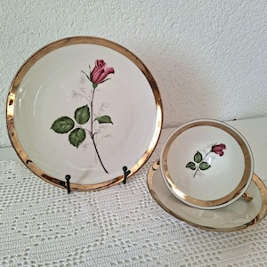 Könnte beinhalten: Vintage weißes Porzellan-Teeservice mit Goldrand und Rosenmotiv. Das Set beinhaltet einen großen Teller, eine Untertasse und eine Teetasse. Die Rose ist tiefrosa mit grünen Blättern.