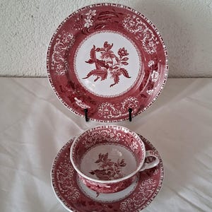 Op de afbeelding: Een keramieken theeservies met een donkerrood en wit bloemmotief in transferdruk. De set bestaat uit een rond bord, een bijpassende schotel en een theekopje. Elk item toont gedetailleerde botanische illustraties en sierlijke randen.
