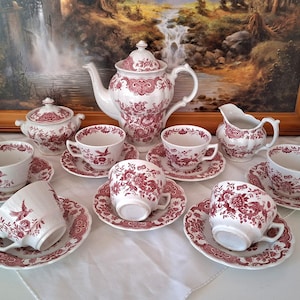 Puede incluir: Un juego de té de porcelana blanca con un patrón floral y de aves en rojo oscuro. El conjunto incluye una tetera con tapa, un azucarero con tapa, una jarra de leche y seis tazas con sus platos, decorados con intrincados motivos botánicos.