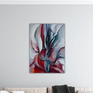 May include: Abstract floral painting with a palette of red, gray, and blue hues. The artwork features soft, flowing shapes and forms, creating a sense of movement and depth. The painting is mounted on a white wall above a sofa.