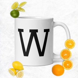 May include: White ceramic mug with a black letter W printed on the front. The mug has a black handle and is surrounded by citrus fruit slices.